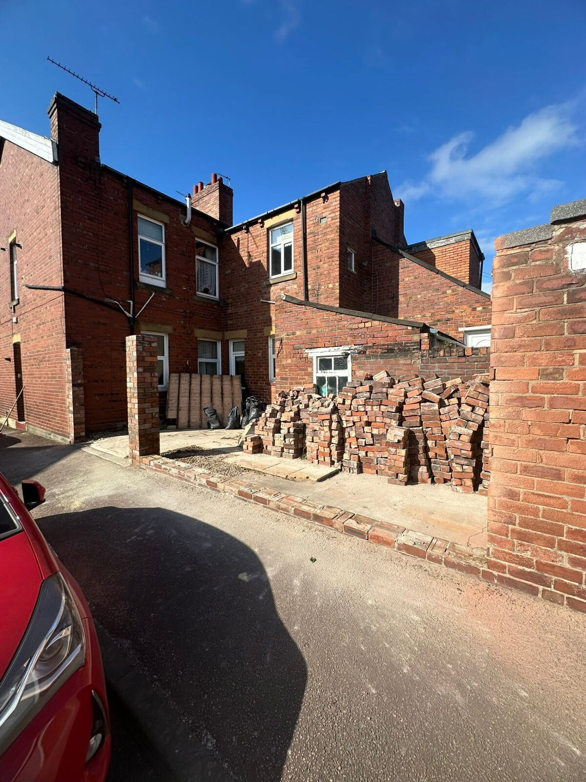 Brick boundary wall under construction in a rear lane with reclaimed bricks stacked